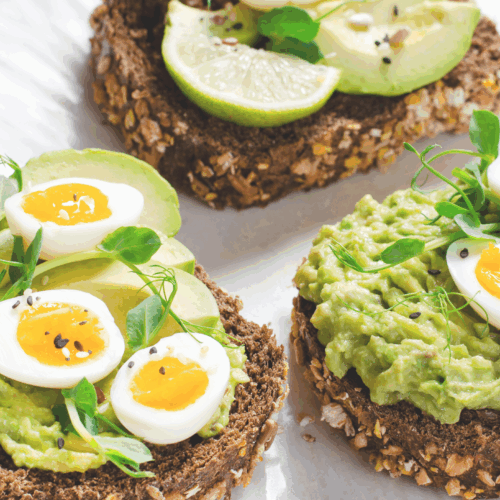 Sliced boiled eggs and creamy avocado arranged elegantly on toasted wholegrain bread, garnished with a sprinkle of black pepper and fresh herbs, served on a ceramic plate.
