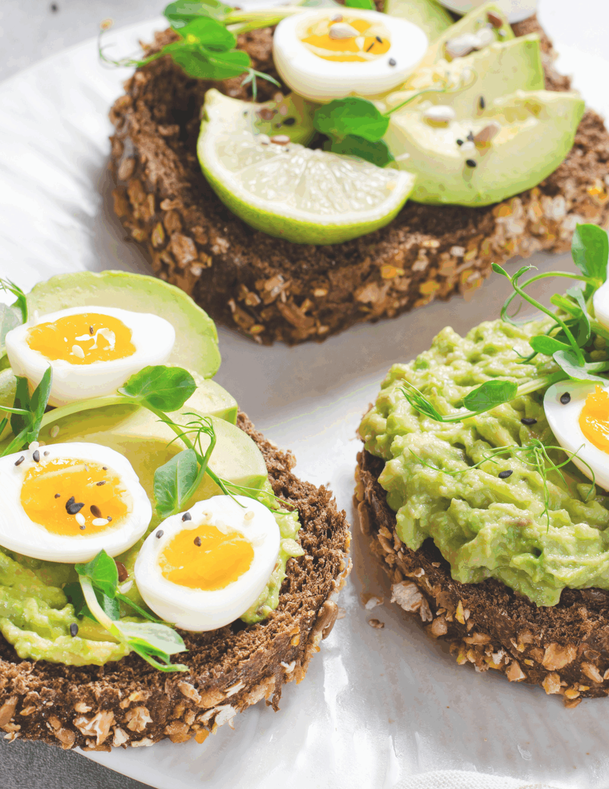 Sliced boiled eggs and creamy avocado arranged elegantly on toasted wholegrain bread, garnished with a sprinkle of black pepper and fresh herbs, served on a ceramic plate.