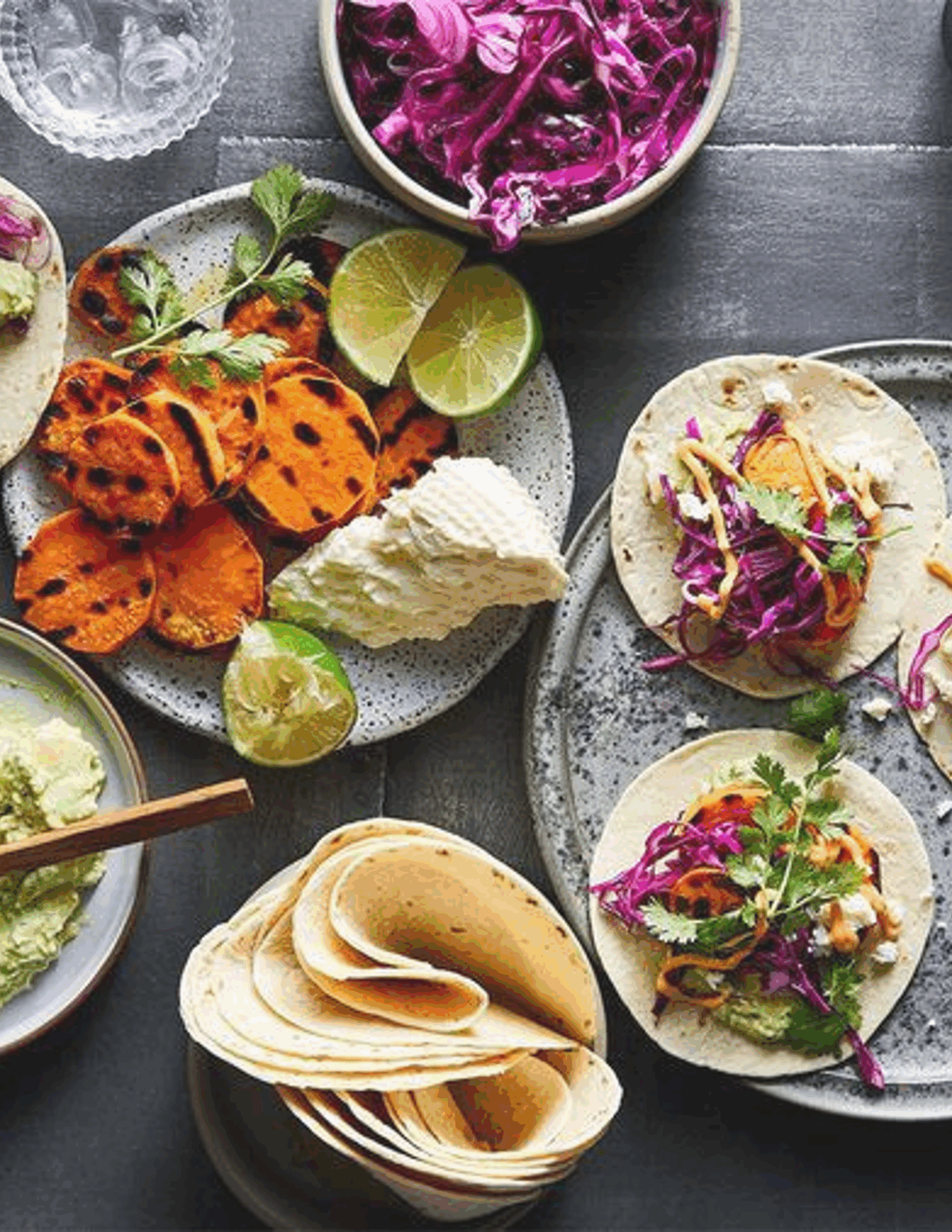 A colourful plate of grilled sweet potato tacos, topped with fresh avocado, tangy feta, crisp red cabbage, and a sprinkle of cilantro, served in warm corn tortillas with a wedge of lime.