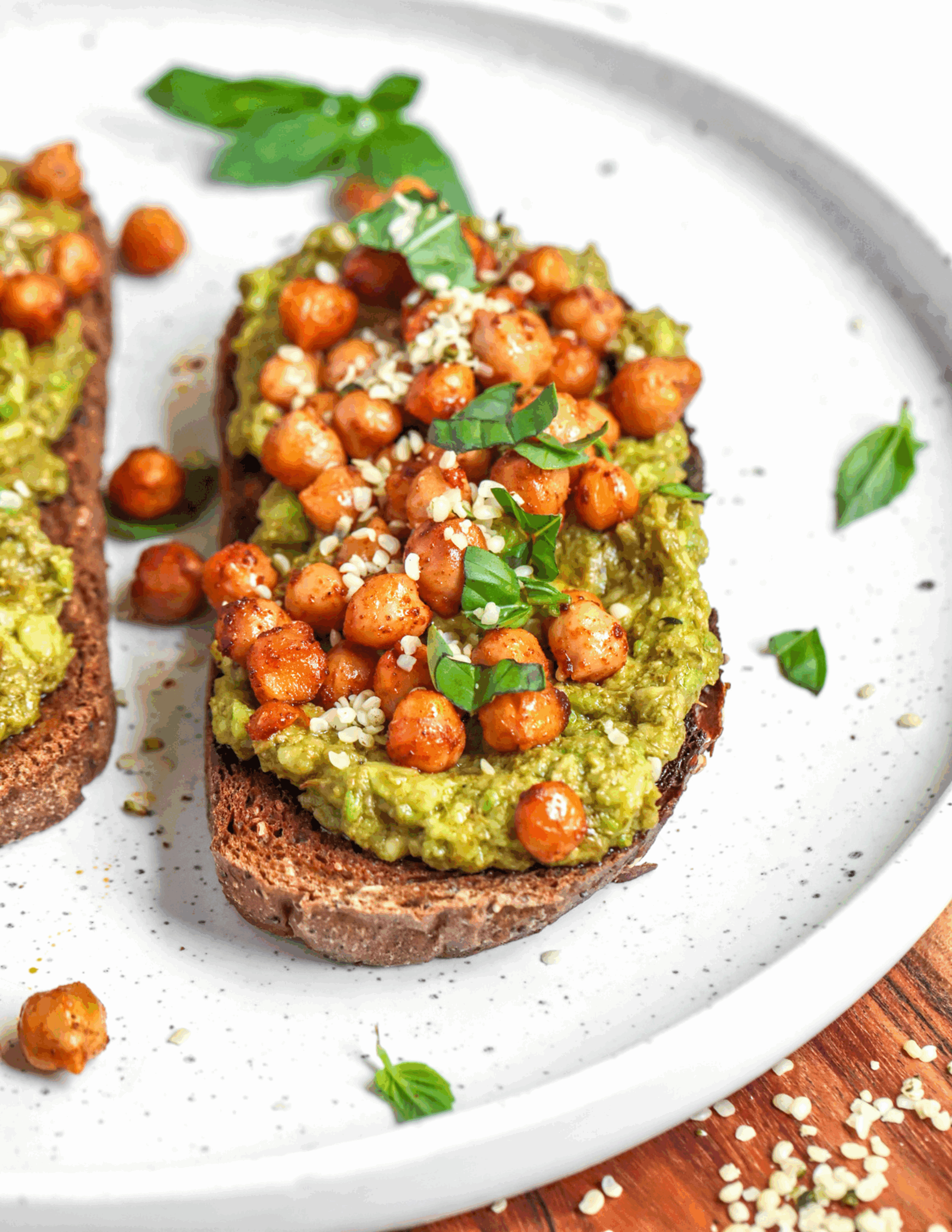 A rustic slice of wholegrain toast topped with creamy pesto chickpea mash, juicy cherry tomatoes, and a sprinkle of fresh basil, served on a ceramic plate for a vibrant, nutritious breakfast.