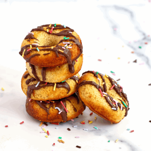 A plate of golden-brown Protein Almond Donuts topped with slivered almonds and dusted with a light touch of powdered sugar, arranged on a rustic wooden table.
