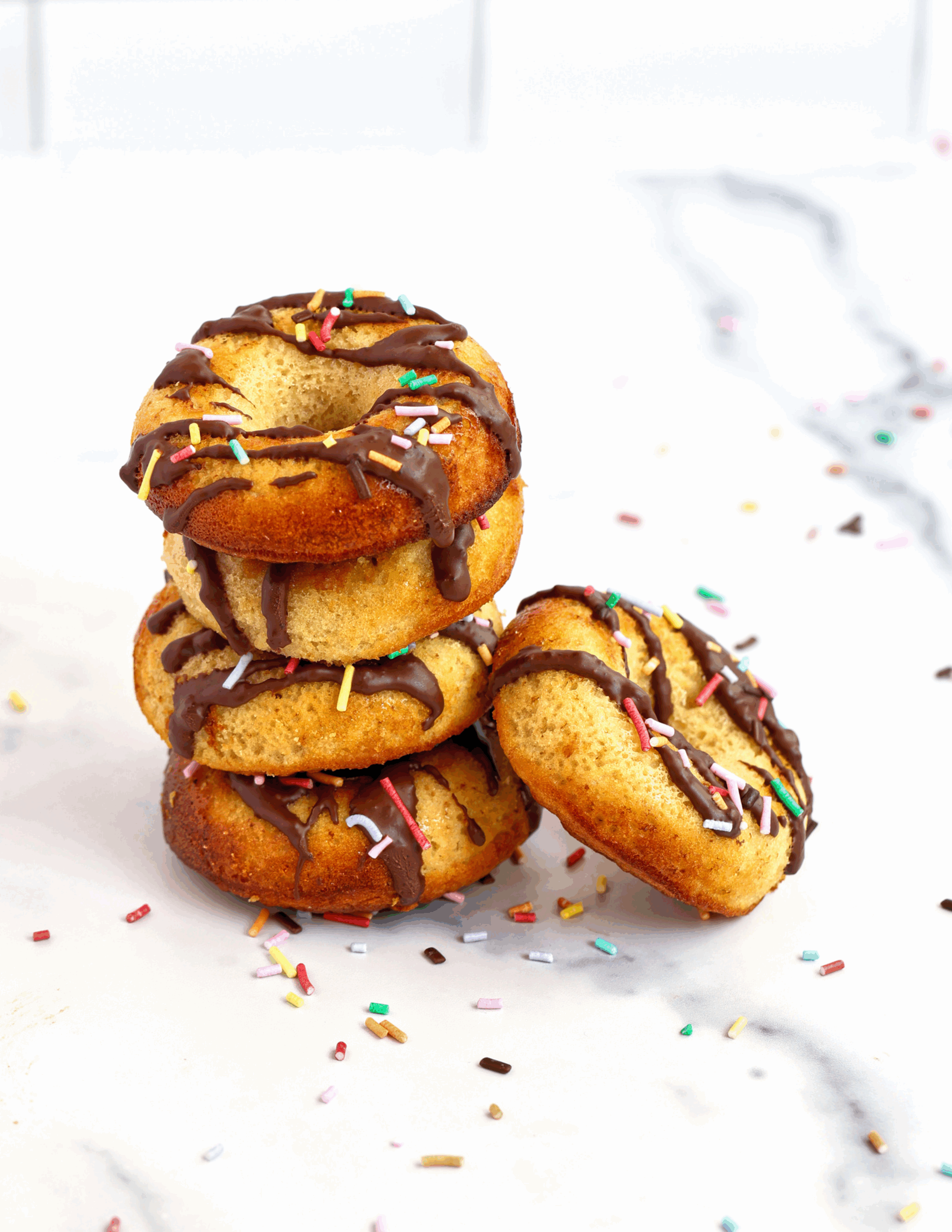 A plate of golden-brown Protein Almond Donuts topped with slivered almonds and dusted with a light touch of powdered sugar, arranged on a rustic wooden table.