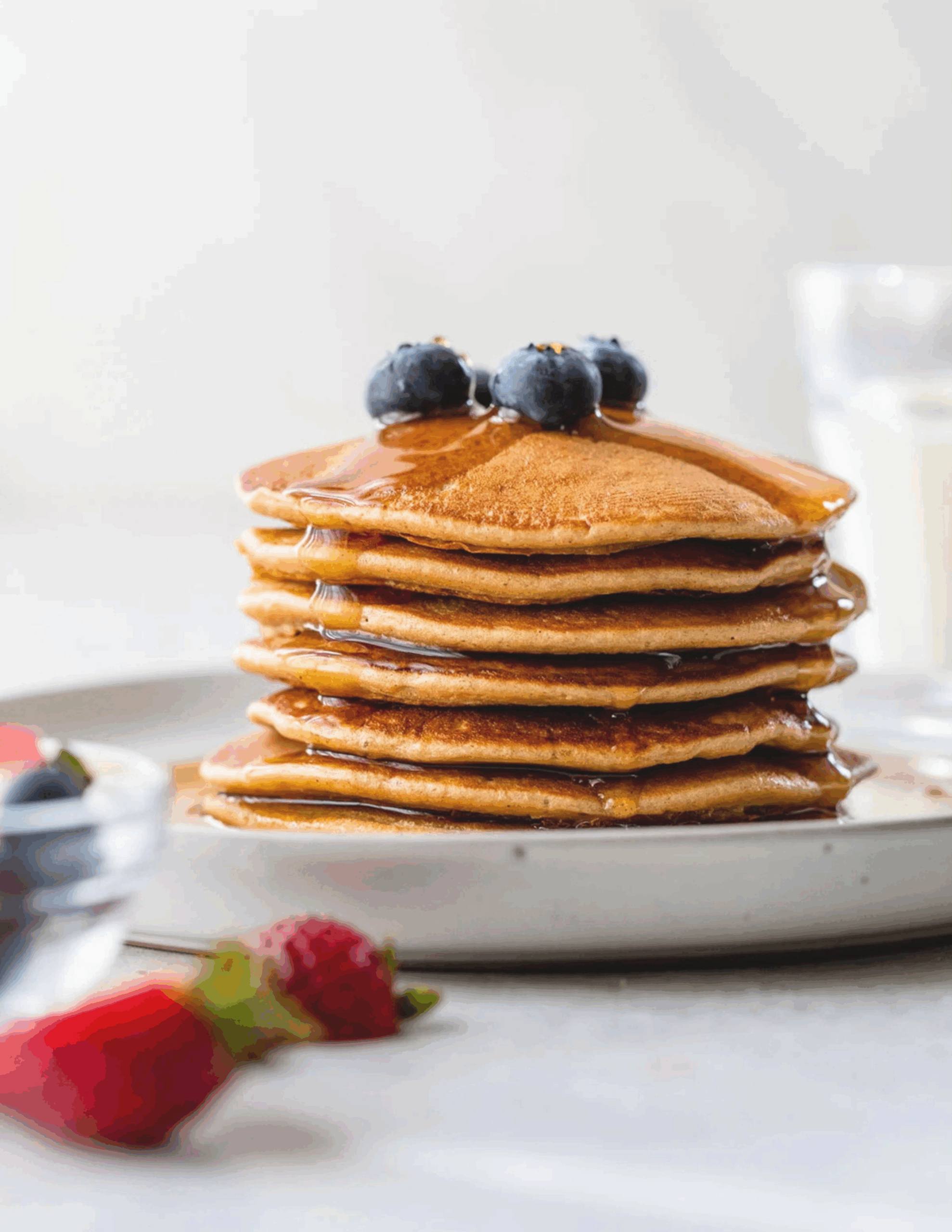 A stack of fluffy Protein Pancakes topped with fresh berries and a drizzle of maple syrup, served on a rustic ceramic plate.