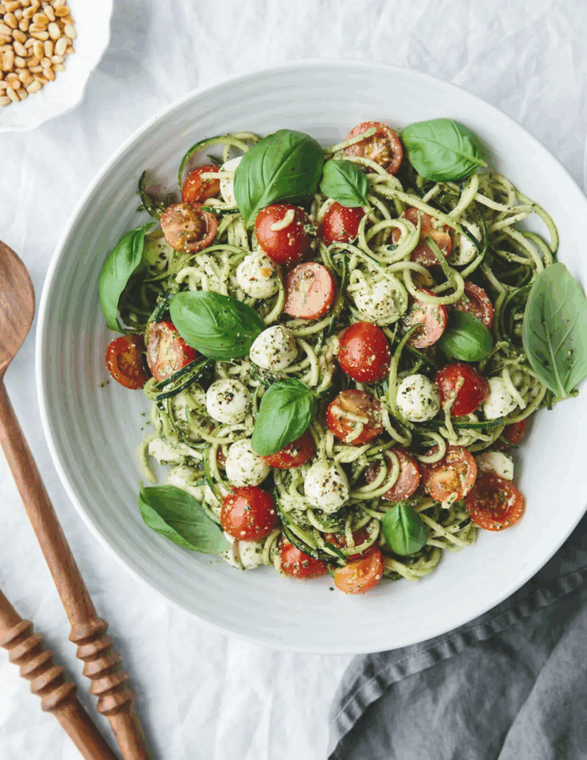 Spiralized zucchini noodles tossed with juicy cherry tomatoes, creamy mozzarella balls, and fresh basil leaves, drizzled with balsamic glaze and arranged on a bright ceramic plate.