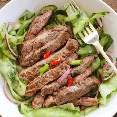 Sliced seared steak atop an Asian-style salad with crunchy vegetables, sesame seeds, and a soy-ginger dressing