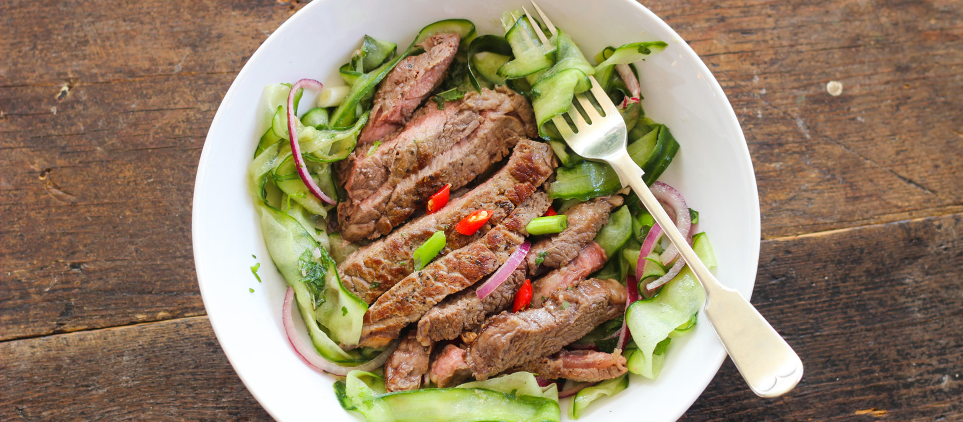 Sliced seared steak atop an Asian-style salad with crunchy vegetables, sesame seeds, and a soy-ginger dressing