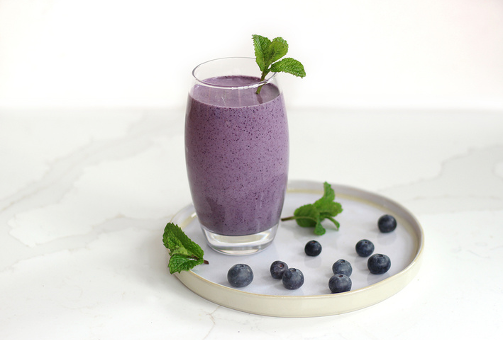 Purple smoothie with mixed berries, banana, and chia seeds in a tall glass with fresh mint garnish
