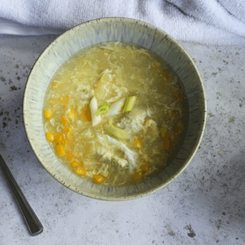 Bowl of chicken and sweetcorn soup with shredded chicken, golden corn kernels, and spring onions