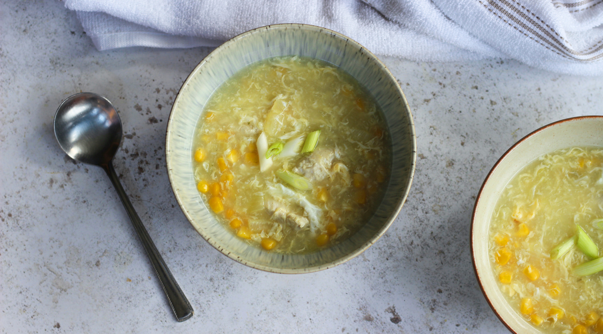 Bowl of chicken and sweetcorn soup with shredded chicken, golden corn kernels, and spring onions