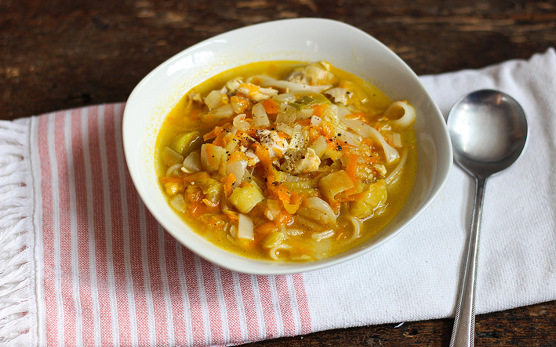 Bowl of clear chicken soup with shredded chicken, mixed vegetables, and noodles topped with herbs