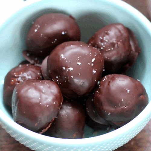 Bite-sized energy balls coated in dark chocolate with chia seeds and nuts on a parchment-lined tray