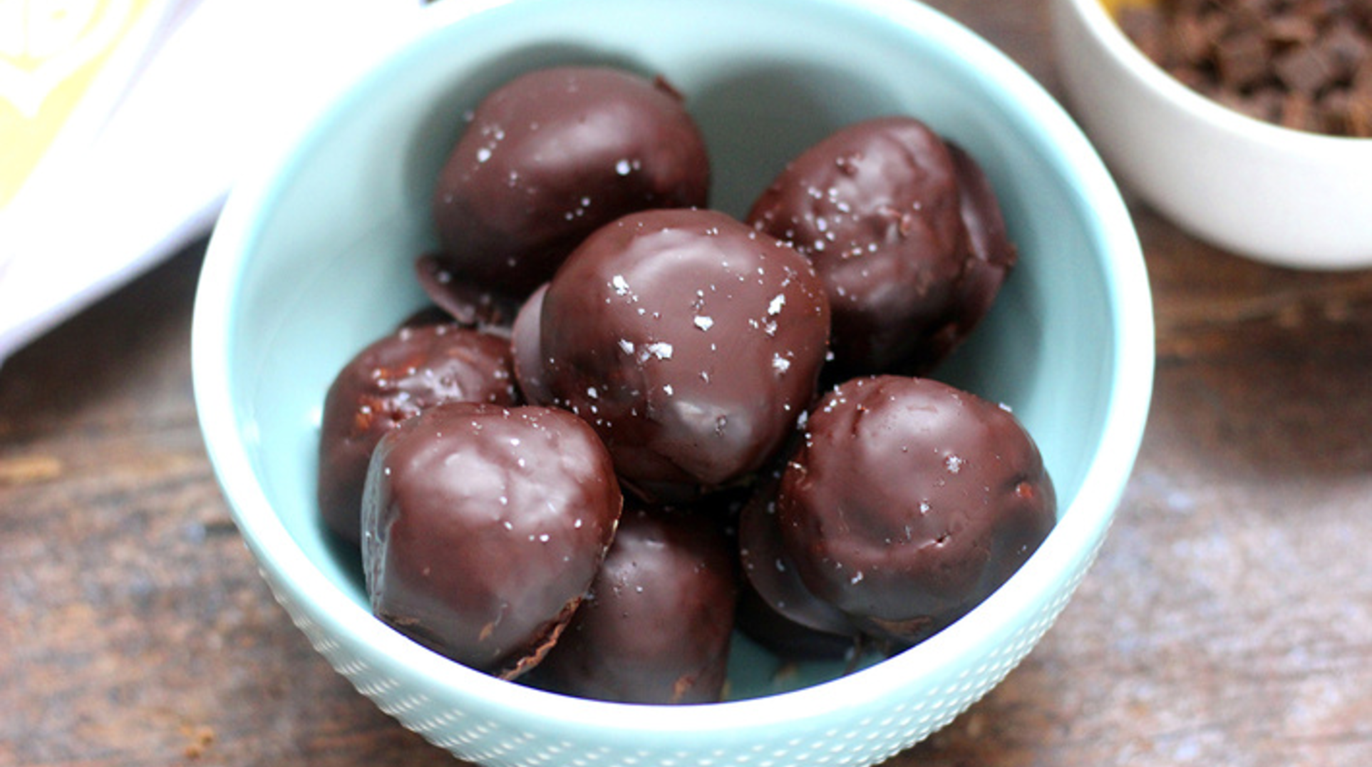 Bite-sized energy balls coated in dark chocolate with chia seeds and nuts on a parchment-lined tray