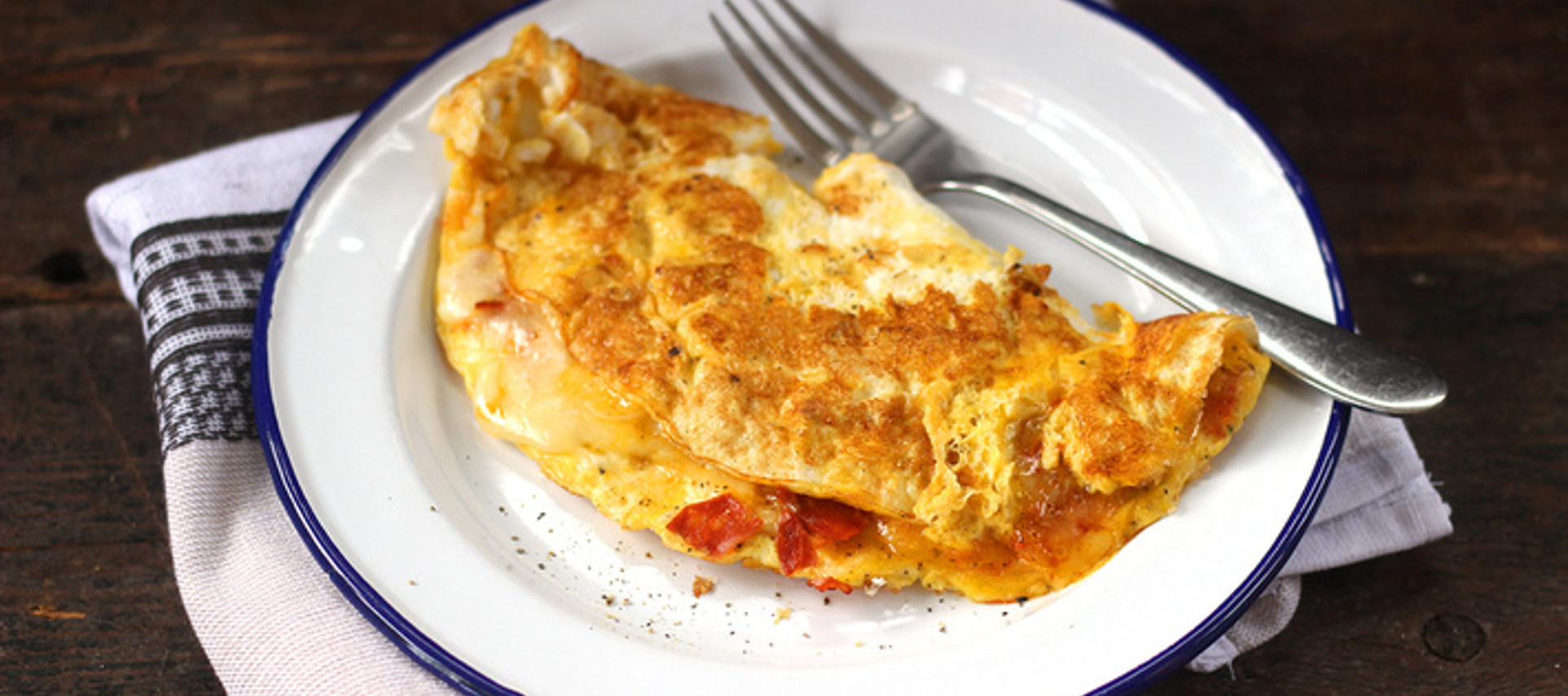 Golden omelette with spicy chorizo slices, melted cheese, and herbs on a ceramic plate