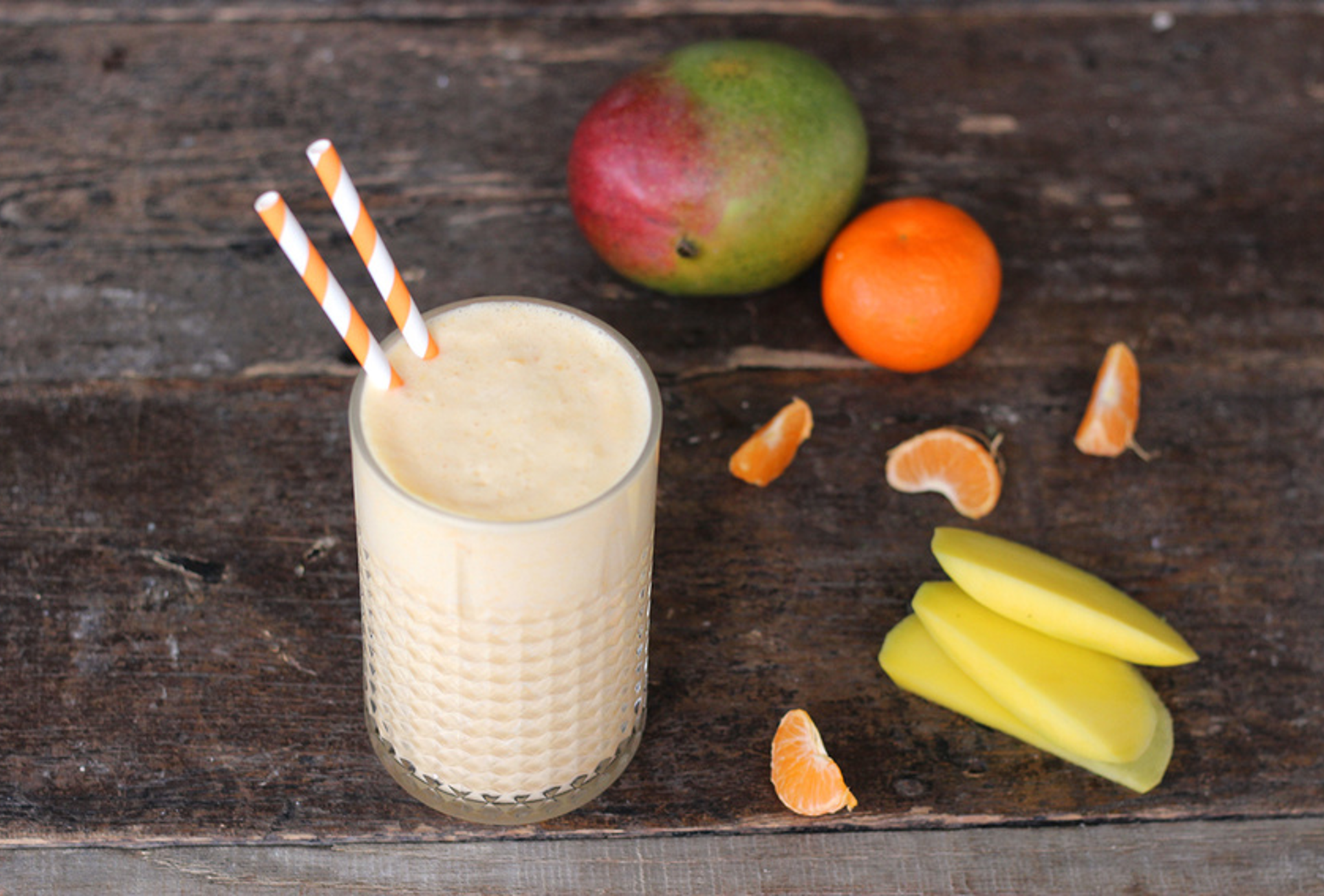 Tropical smoothie with mango chunks, orange segments, and banana in a chilled glass with citrus zest garnish