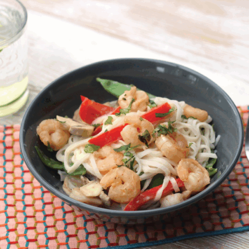 Stir fry with prawns, vegetables, and a coconut lemongrass sauce in a wok garnished with fresh herbs