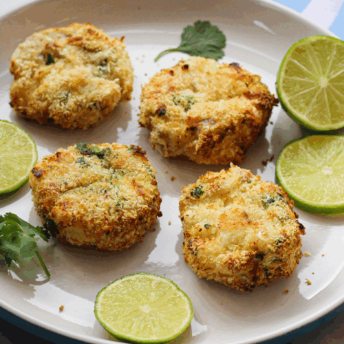 Golden fishcakes with crispy edges, served with lime wedges and fresh herbs on a ceramic plate