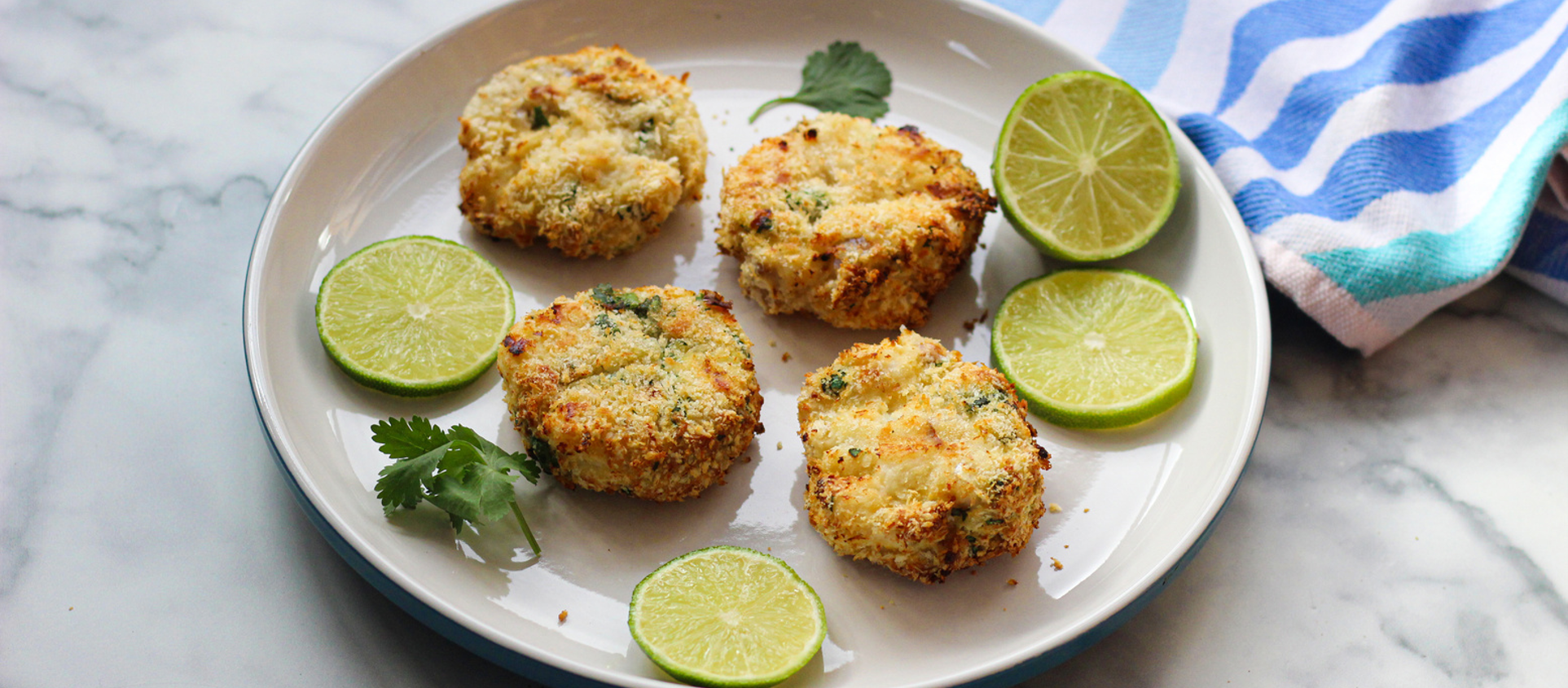 Golden fishcakes with crispy edges, served with lime wedges and fresh herbs on a ceramic plate