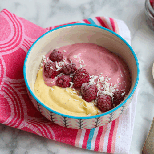 Bowl of creamy yogurt layered with mango chunks, fresh raspberries, and chia seeds on a vibrant background