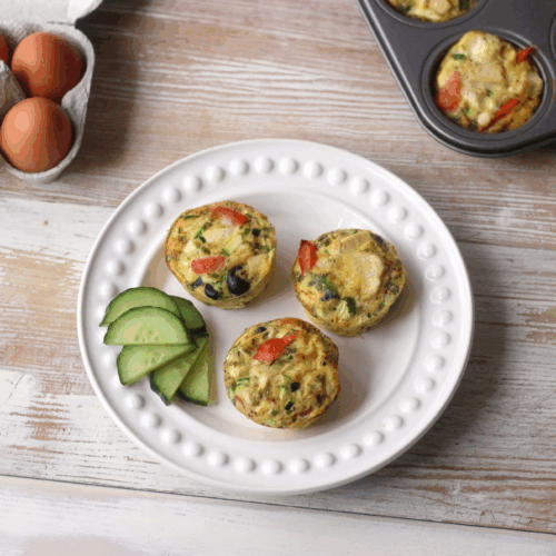 Savoury muffins with sun-dried tomatoes, olives, feta, and herbs stacked on a rustic board