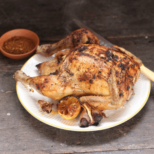Whole roast chicken coated with Moroccan spices, garnished with herbs and lemon slices on a rustic platter