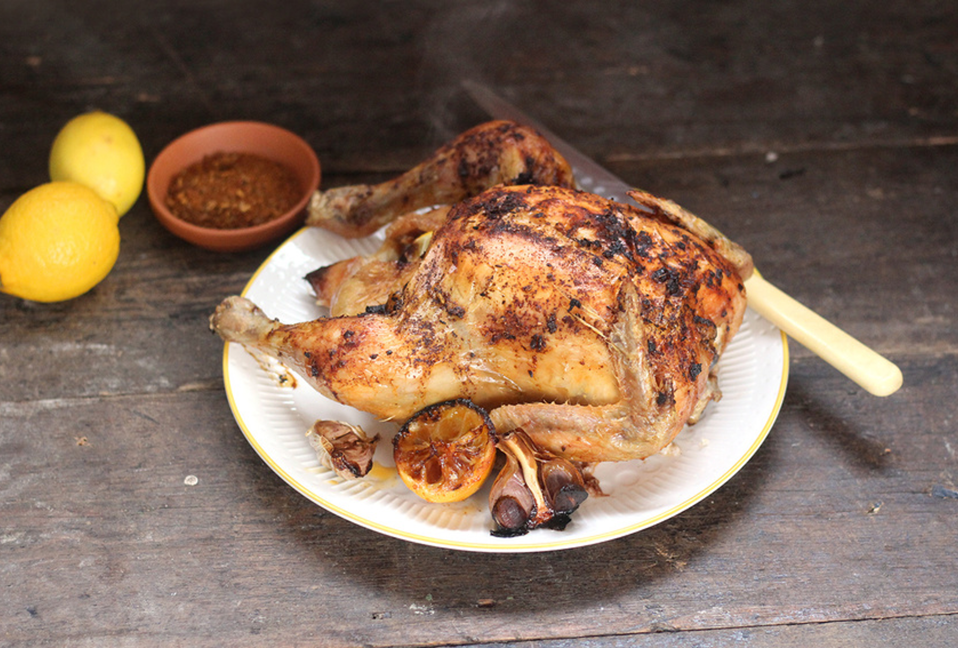 Whole roast chicken coated with Moroccan spices, garnished with herbs and lemon slices on a rustic platter