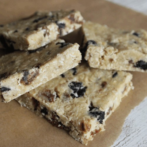 Round oaty snack balls made with oats, nut butter, and dried fruit, stacked on parchment paper