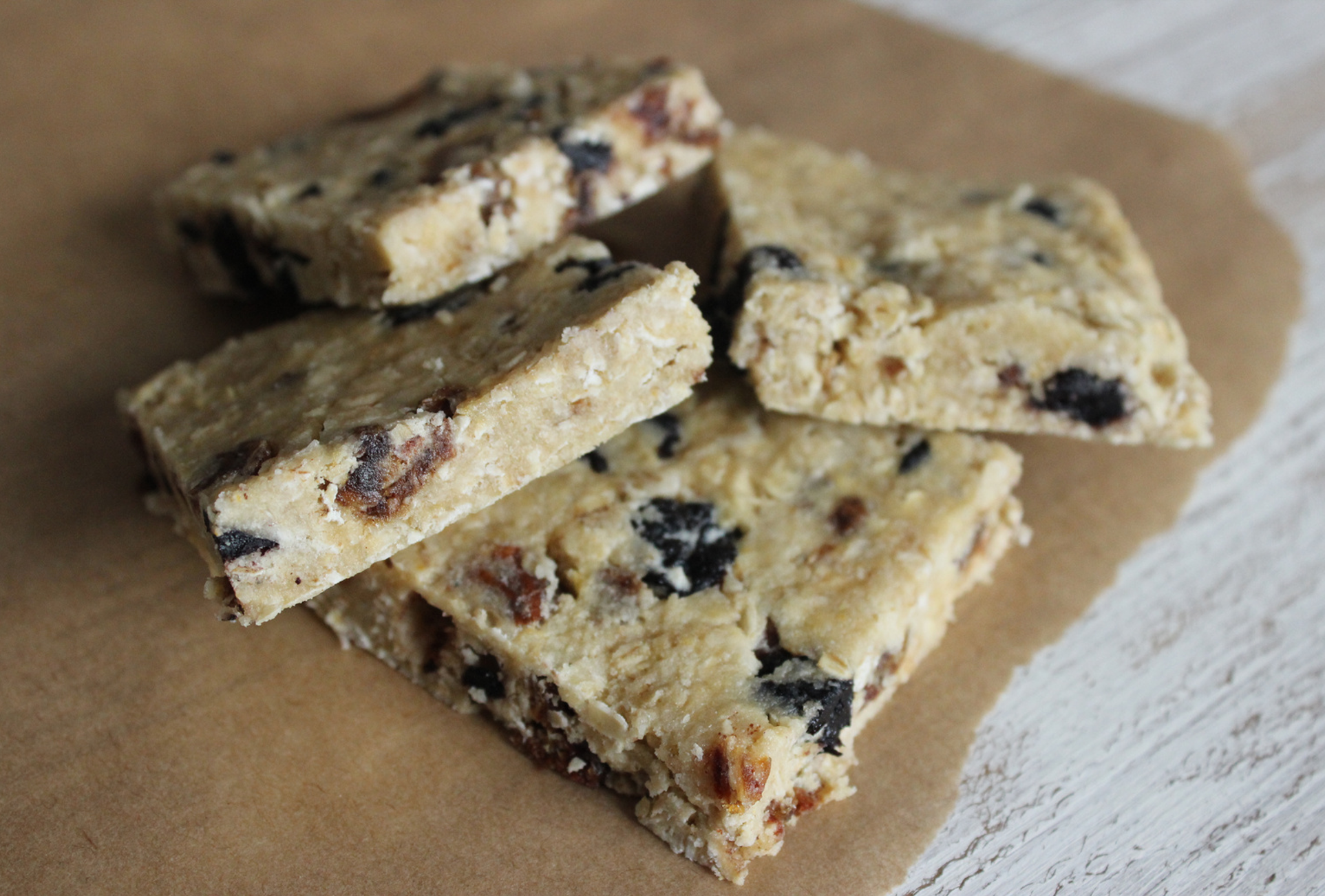 Round oaty snack balls made with oats, nut butter, and dried fruit, stacked on parchment paper