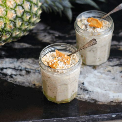 Jar of overnight oats layered with mango, pineapple, coconut milk, and chia seeds, topped with shredded coconut and lime zest