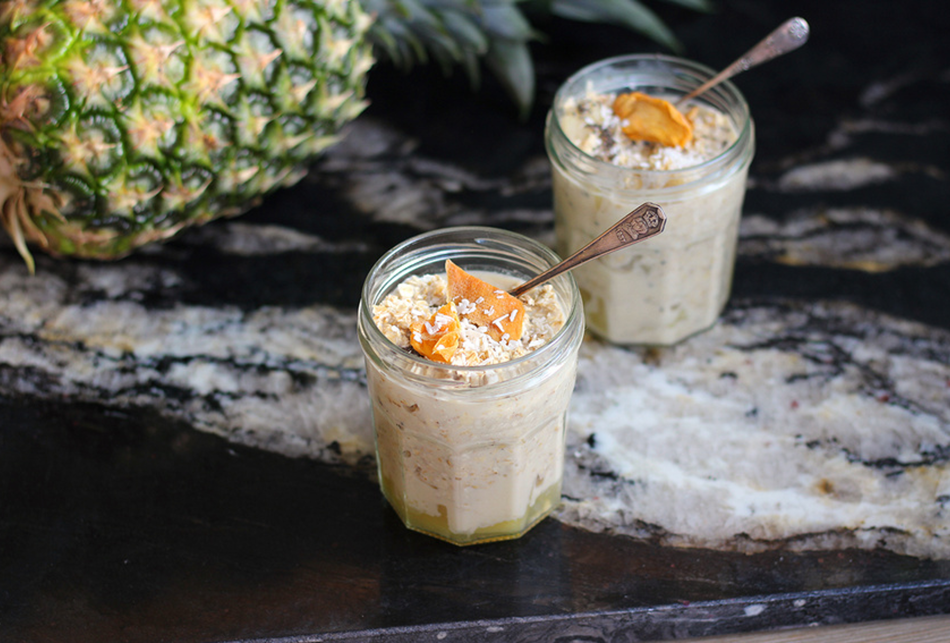 Jar of overnight oats layered with mango, pineapple, coconut milk, and chia seeds, topped with shredded coconut and lime zest