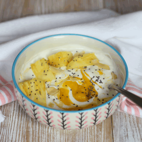 Bowl of protein yogurt topped with mango, pineapple, shredded coconut, and chia seeds
