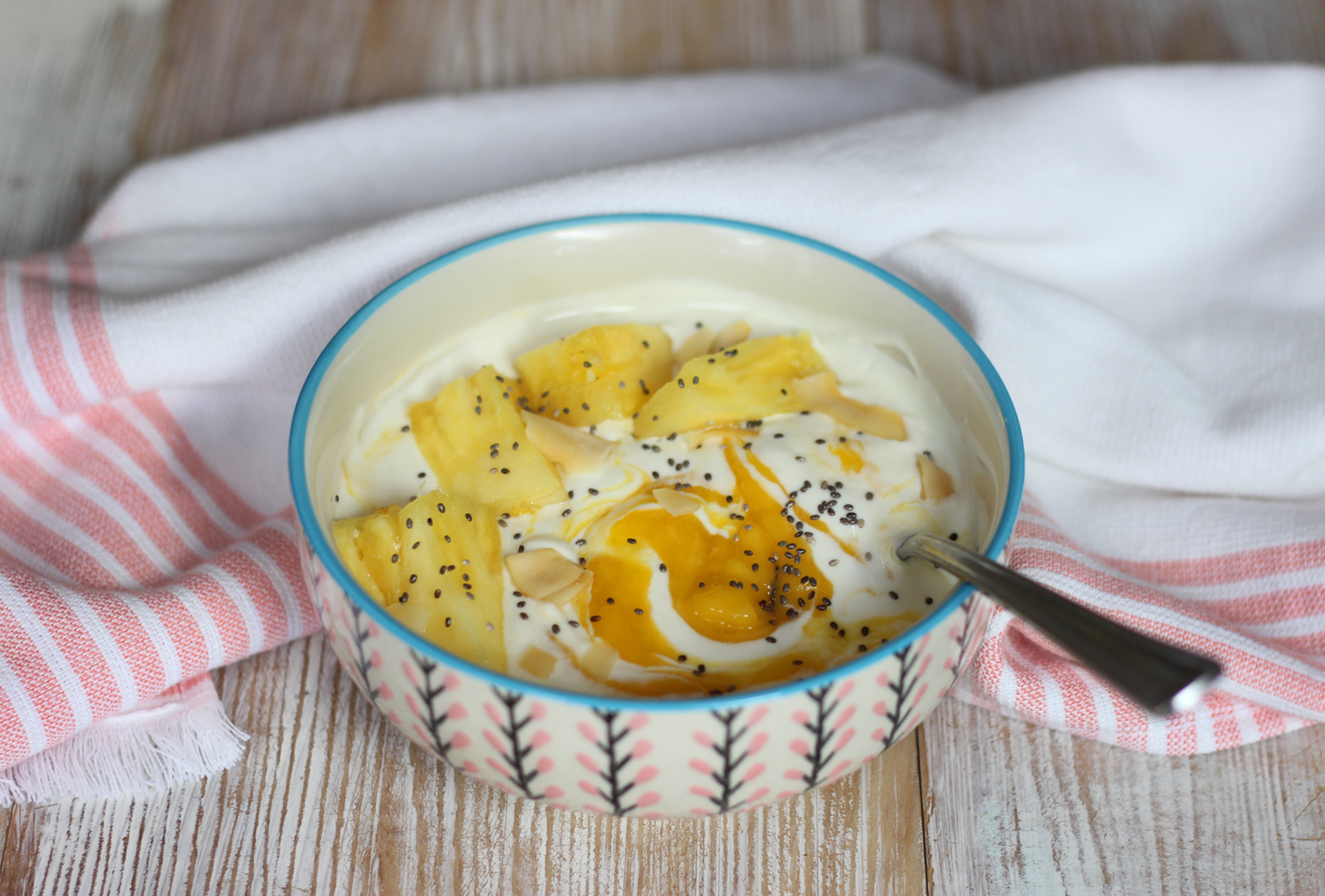 Bowl of protein yogurt topped with mango, pineapple, shredded coconut, and chia seeds