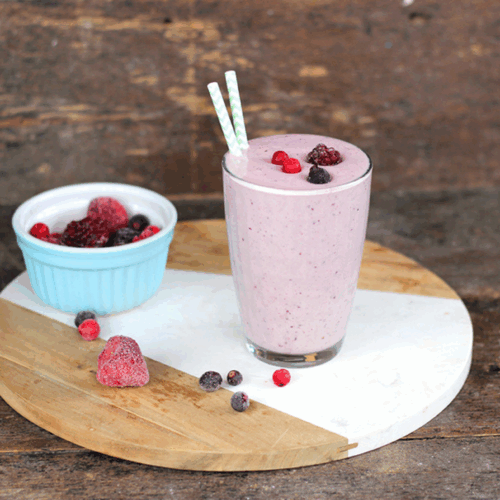 Creamy berry smoothie in a glass with vanilla pod garnish, topped with mixed berries and mint leaves