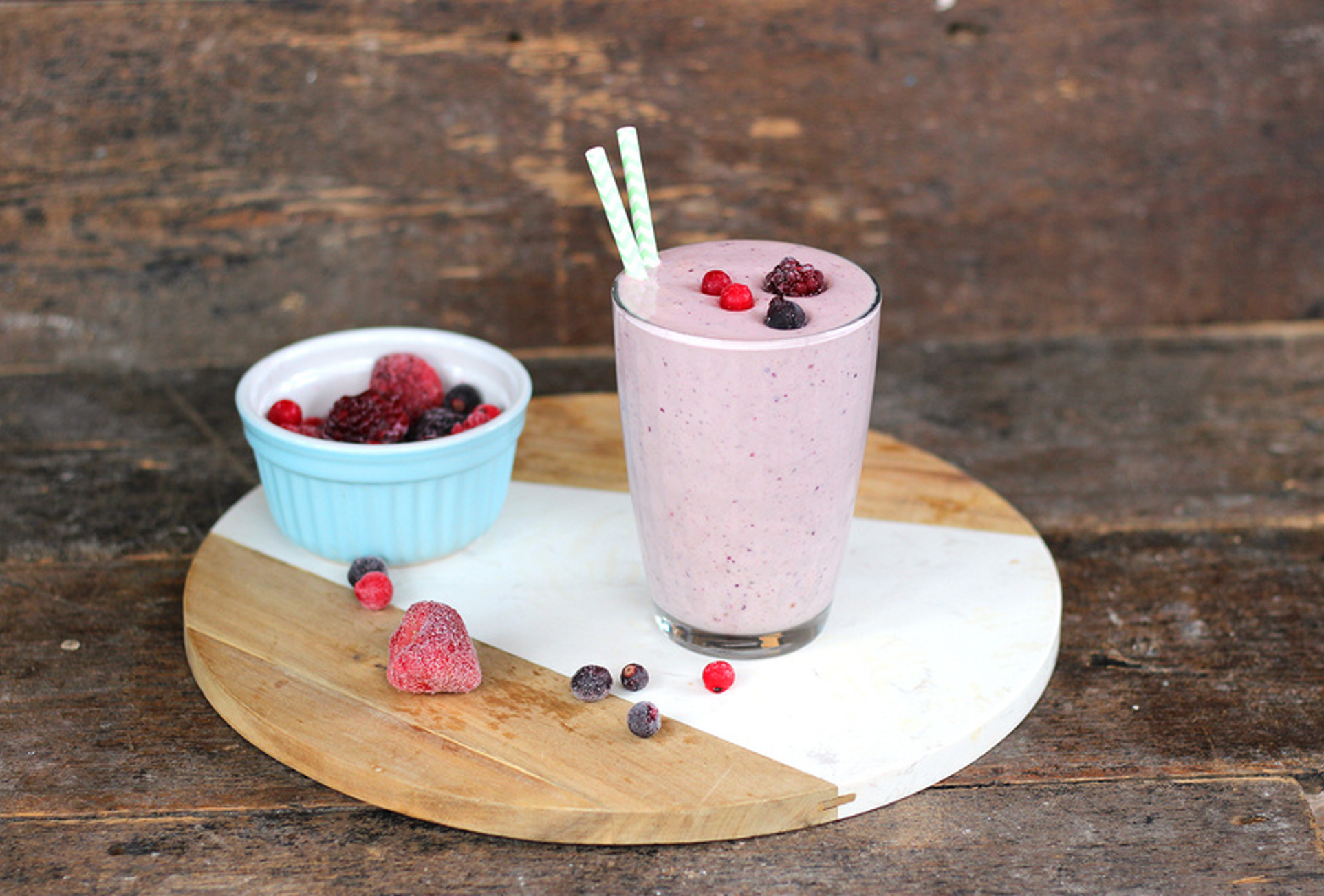 Creamy berry smoothie in a glass with vanilla pod garnish, topped with mixed berries and mint leaves