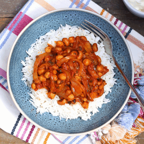 Bowl of vegetarian chilli with beans and chickpeas in rich tomato sauce, garnished with avocado and herbs