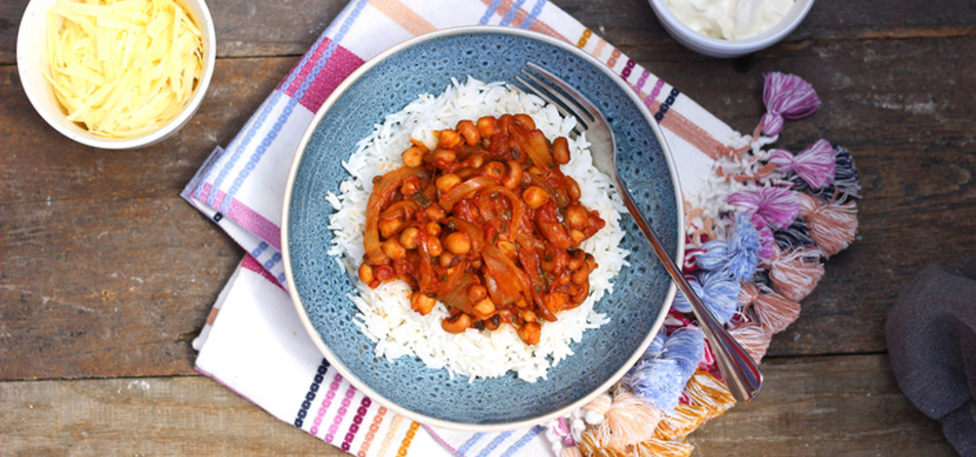 Bowl of vegetarian chilli with beans and chickpeas in rich tomato sauce, garnished with avocado and herbs